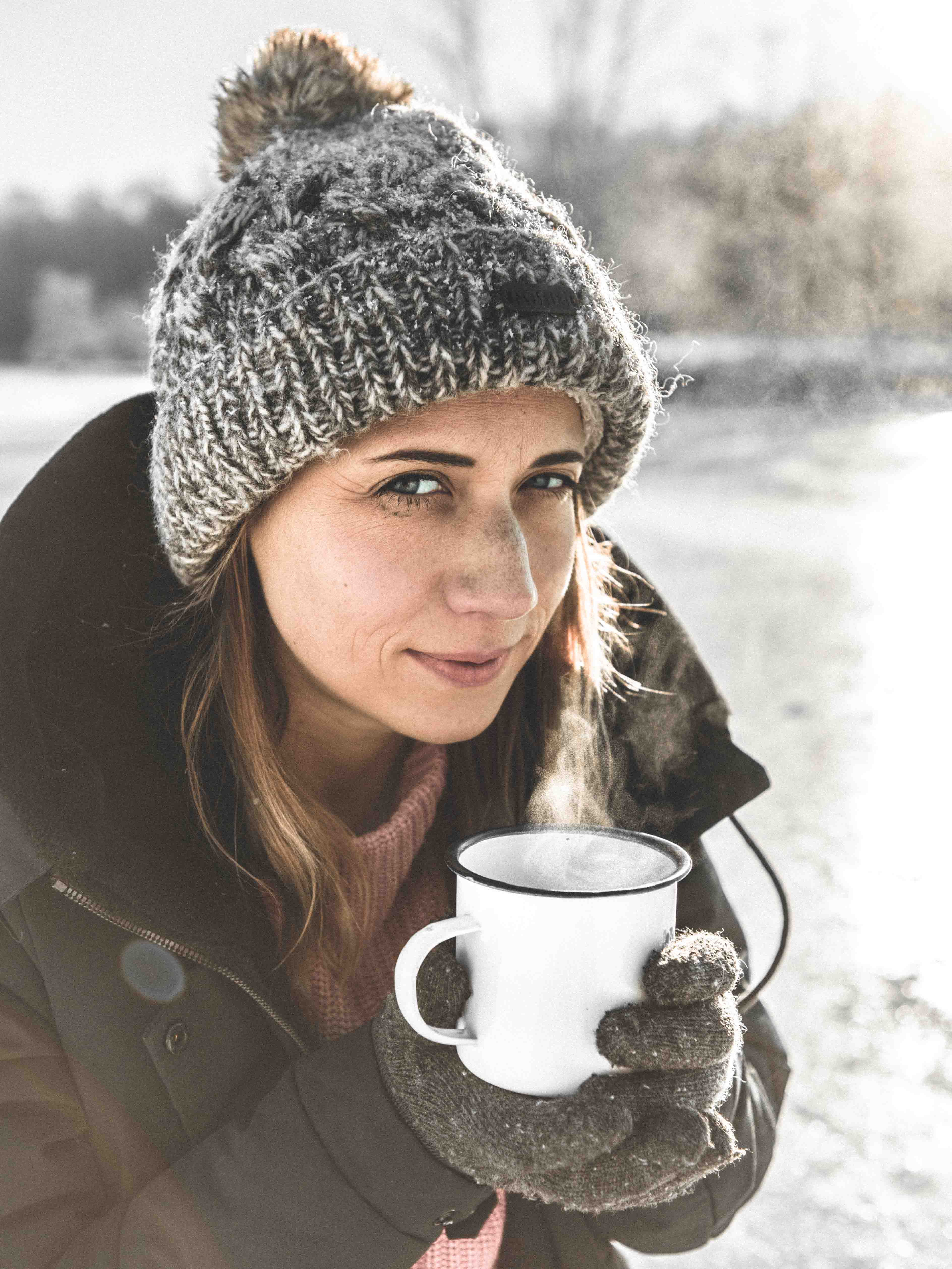 Frau mit Mütze hält eine Tasse dampfenden Tee