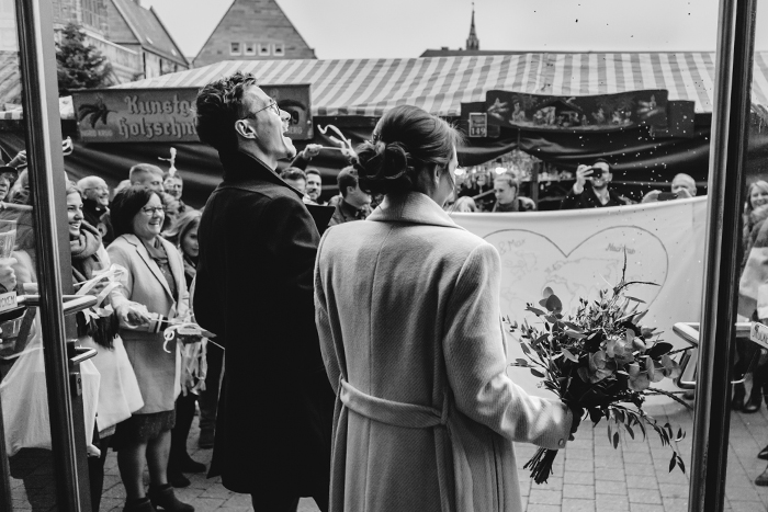 Schwarz-Weiß-Bild: Rückenansicht von einem Brautpaar, das von Spalierstehern empfangen wird