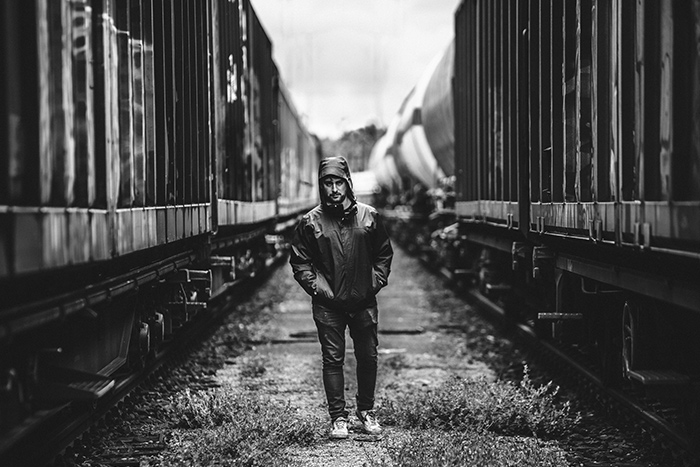 Schwazr-Weiß-Portrait junger Mann zwischen zwei Güterzügen