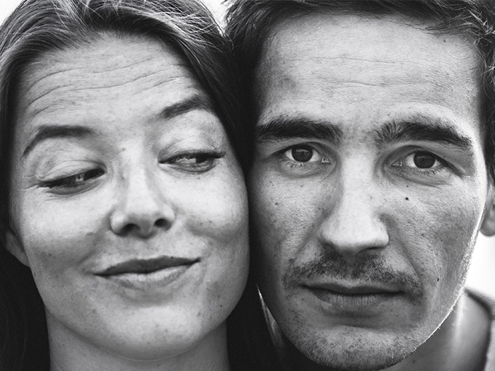 Nahaufnahme junges Paar Kopf an Kopf. Sie grinst verschmitzt. Schwarzweiss-Fotografie