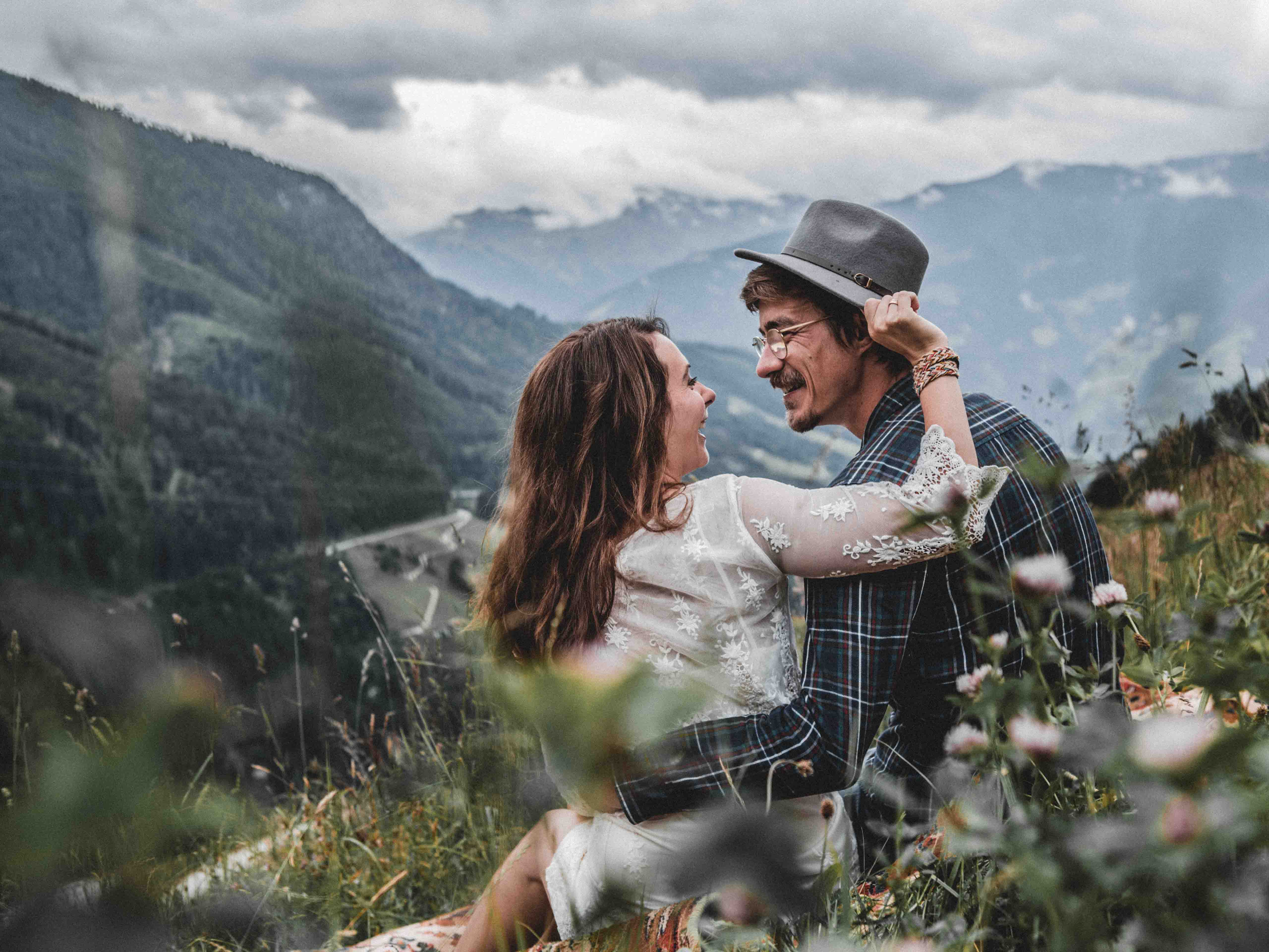 Paar sitzt mit Rücken zur Kamera vor Bergpanorama. Er trägt Hut