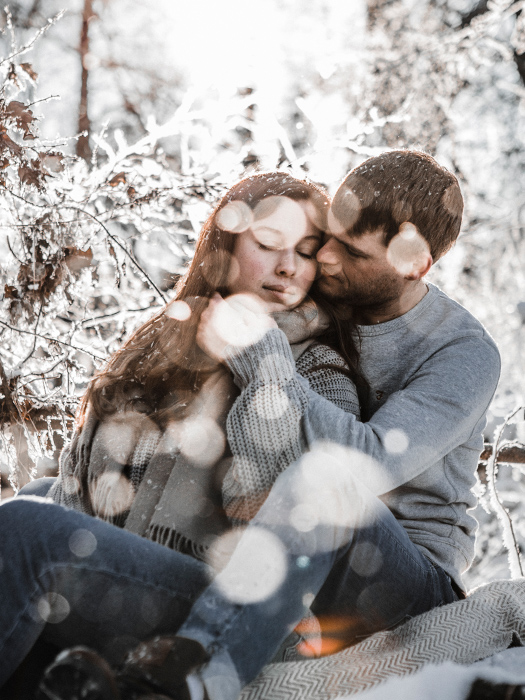 Junges Paar schmust innig umarmt umgeben von Winterlandschaft