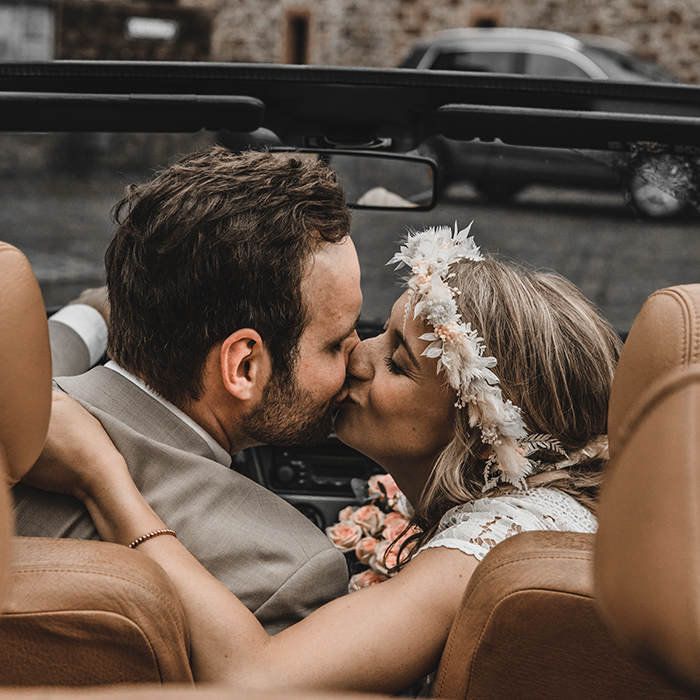 Hochzeitspaar sitzt im Brautauto und küsst sich