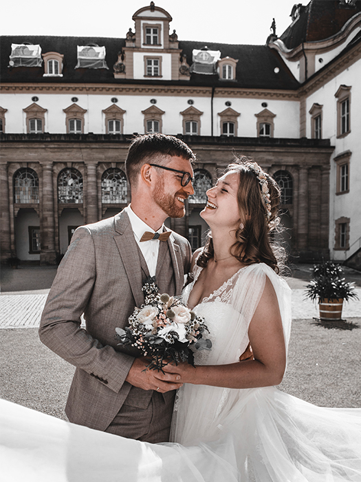 Brautpaar vor Residenz schaut sich lachend an