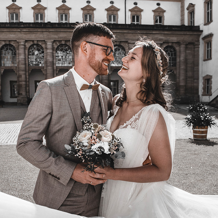 Brautpaar steht vor der Residenz und strahlt sich an.