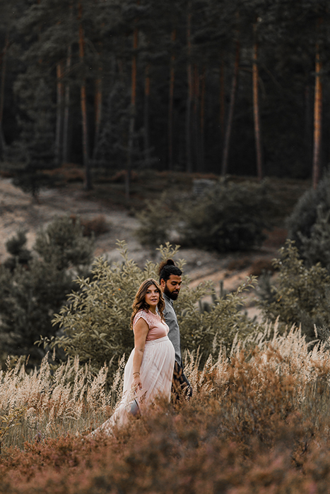 Werdende Mutter mit Babybauch geht mit ihrem Mann Hand in Hand durch die Heide