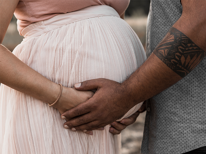 Ausschnitt Babybauch. Beide werdenden Eltern fassen zärtlich an den BAuch der Frau