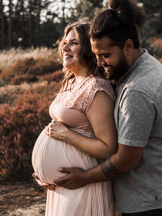 Babybauchshooting. Werdende Mami hält ihren Bauch. Ihr Mann fasst seiner Frau zärtlich an den Babybauch