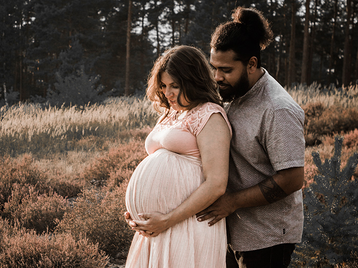 Babybauchshooting. Werdende Mami hält ihren Bauch. Ihr Mann steht hinter ihr