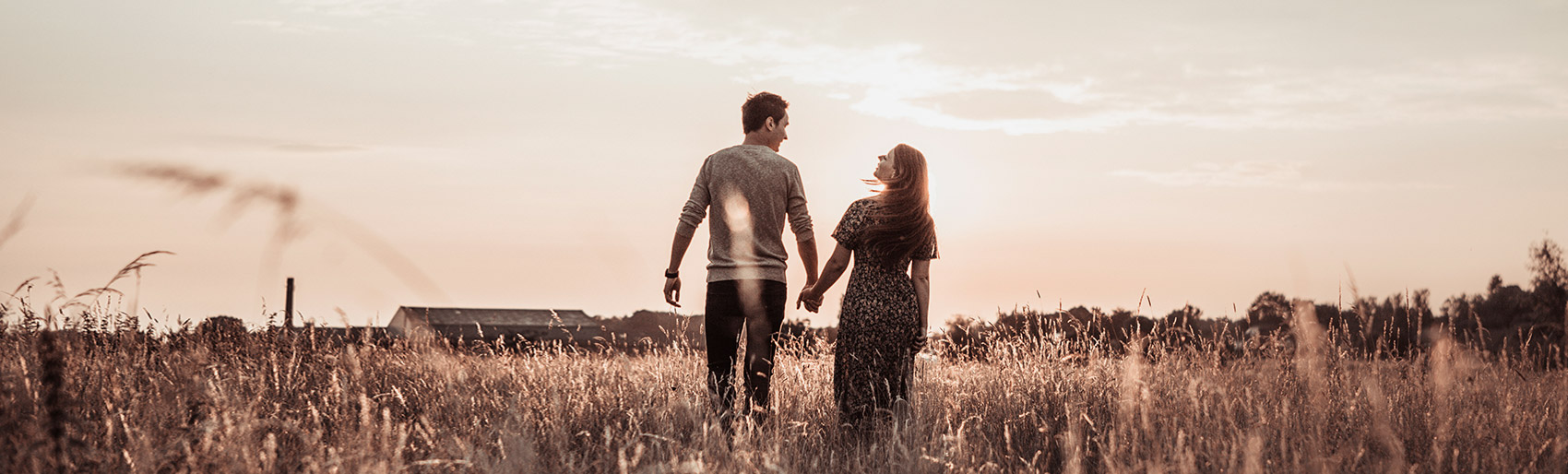 Paar spaziert Hand in Hand über ein Feld in der untergehenden Sonne