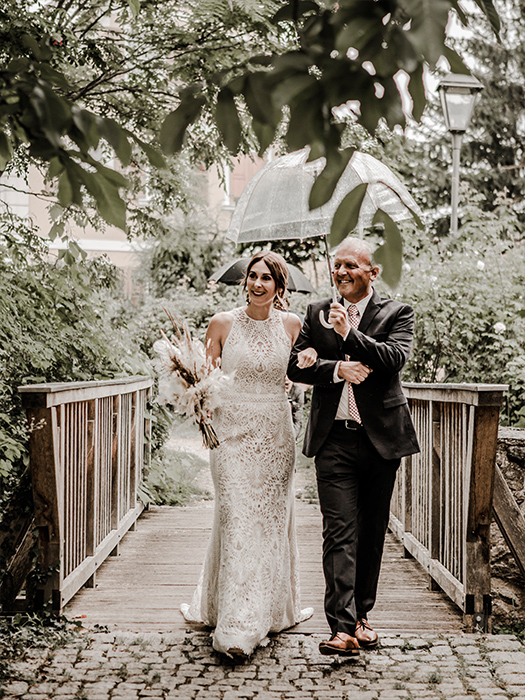 Braut wird von ihrem Vater zum Altar gebracht. Er hält ihr einen Regenschirm
