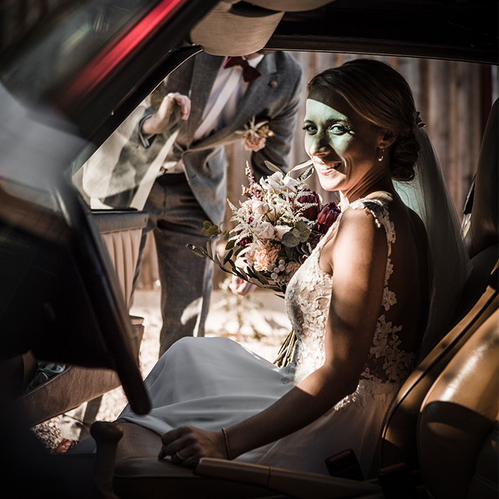 Braut sitzt im Hochzeitsauto. Bräutigam öffnet ihr die Autotüre