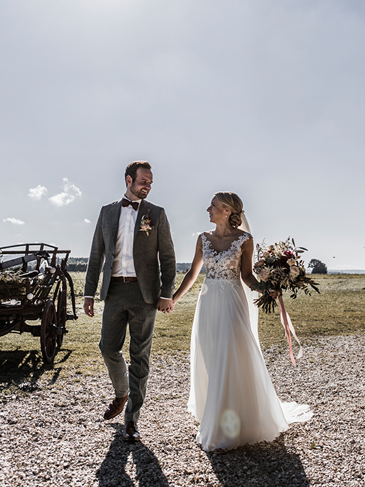 Brautpaarshooting: Hochzeitspaar geht Hand in Hand über einen Feldweg und schaut sich dabei an.