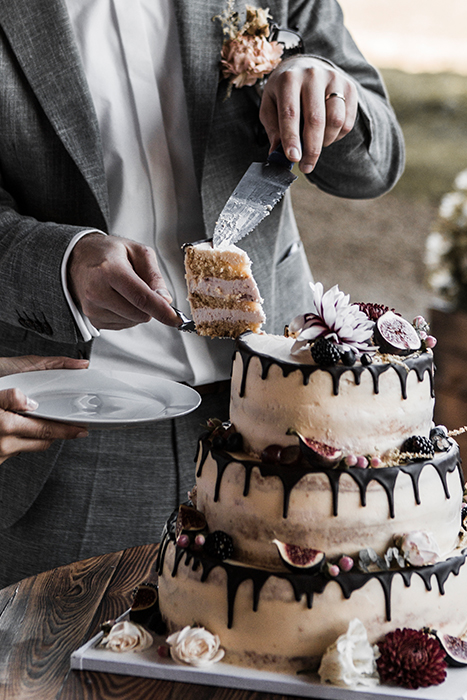 Bildausschnitt auf dem der Bräutigam der Braut ein Stück Hochzeitstorte auf den Teller legt