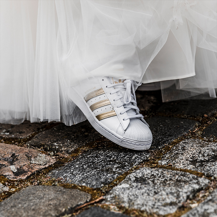 Detailaufnahme weißer Turnschuh blitzt unter Brautkleid hervor
