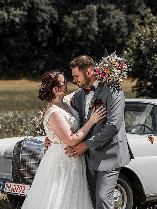 Brautpaar vor Hochzeitsauto schaut sich an.