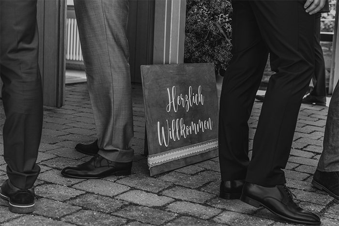 Schwarz-weiß Bild von einem Herzlich-Willkommen-Schild vor dem Männer in Anzügen stehen