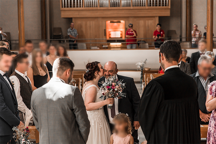 Braut wird von Vater zum Traualtar gebracht. Sie küsst ihn zum Dank