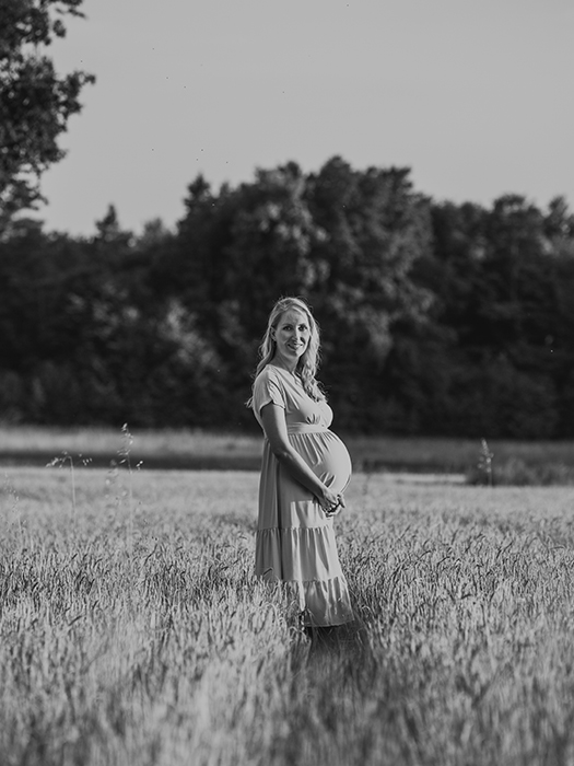 Schwangere Frau im Kornfeld hält ihren Babybauch