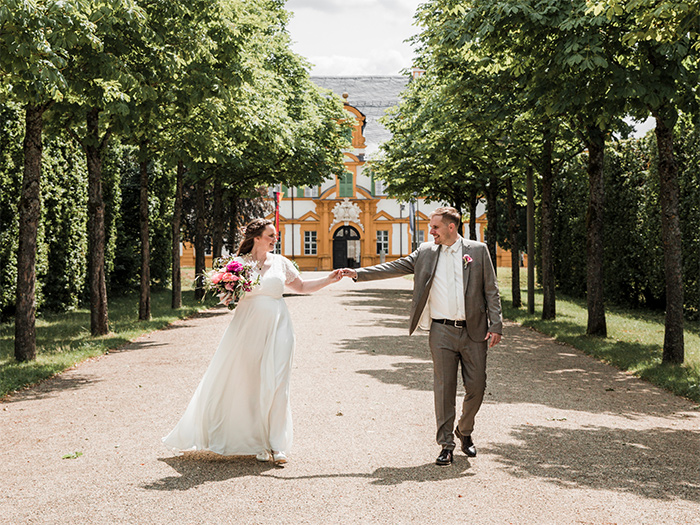 Brautpaar läuft Händchenhaltend durch einen Schlosspark