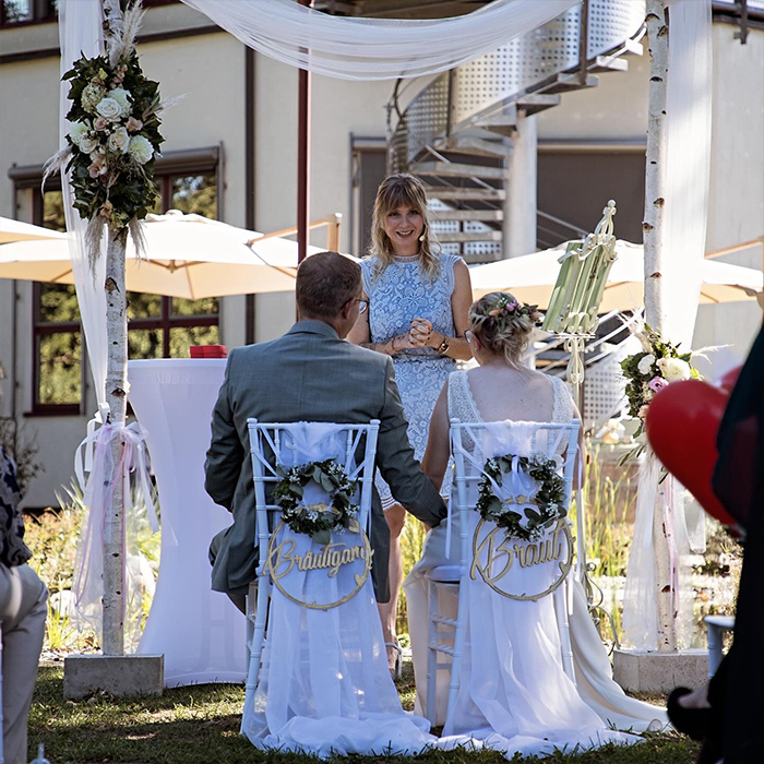 Traurednerin traut Hochzeitspaar das auf Stühlen sitzt